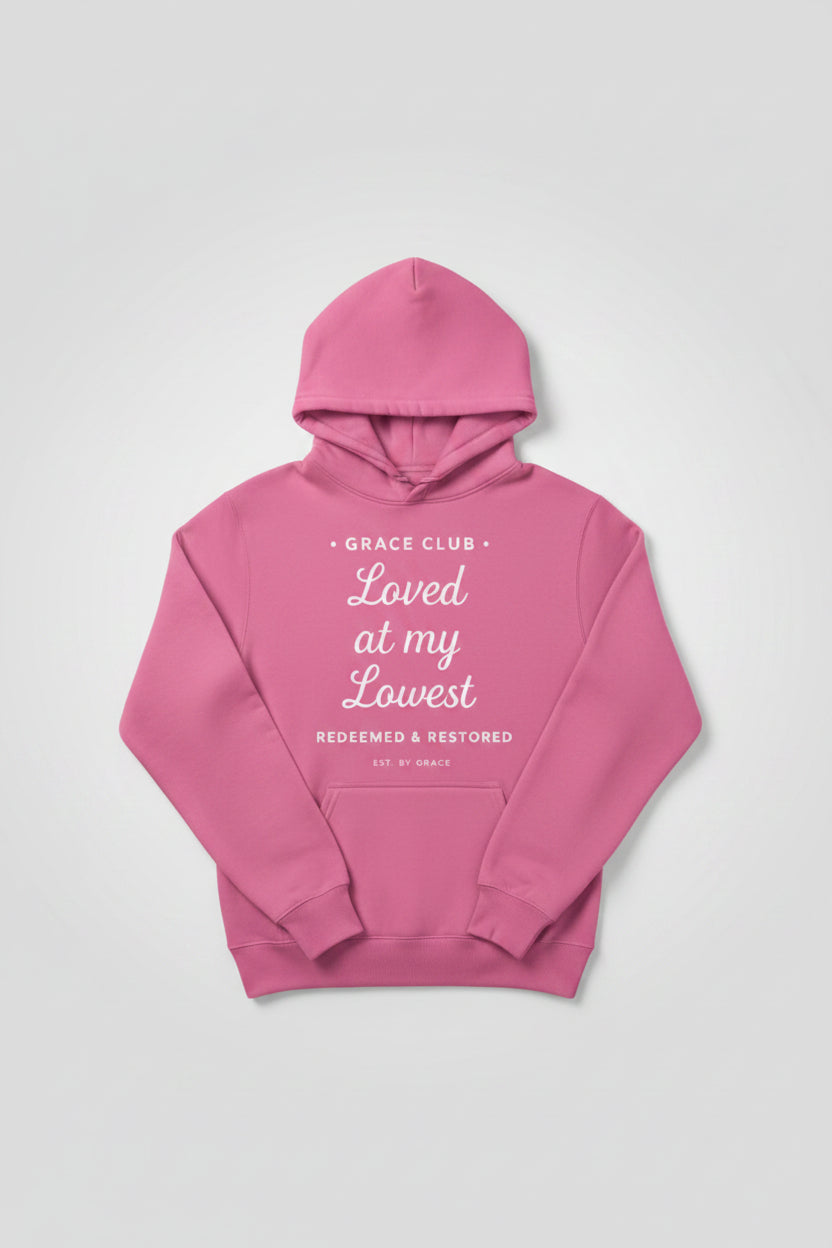 Pink hoodie with text 'Grace Club Loved at my Lowest Redeemed & Restored EST. BY GRACE' on a white background
